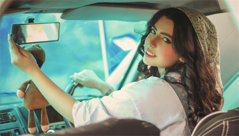 Teen in car drivers seat looking back in rear view mirror